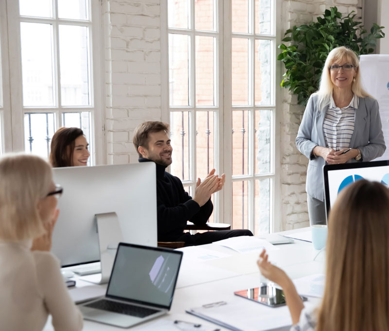 5 Personen sitzen am Schreibtisch und tauschen sich aus.